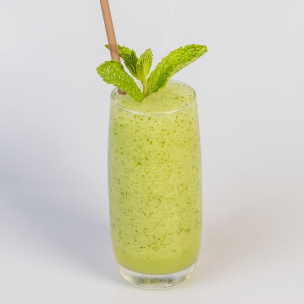 Refreshing green slushy drink with a straw and mint garnish, against a white background.
