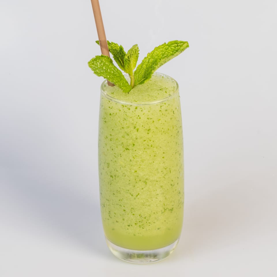 Refreshing green slushy drink with a straw and mint garnish, against a white background.