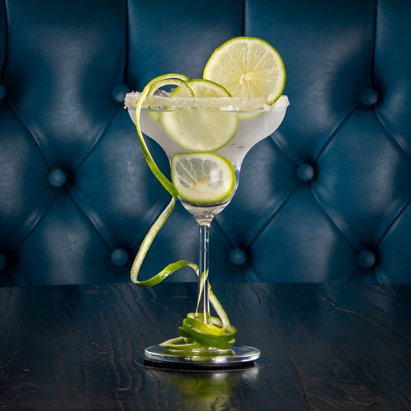 Margarita with lime slices and a sugar-salted rim on a dark table with a blue tufted background.