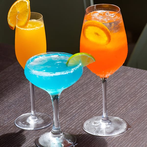 Three vibrant cocktails, two orange and one blue, garnished with citrus slices on a dark table.