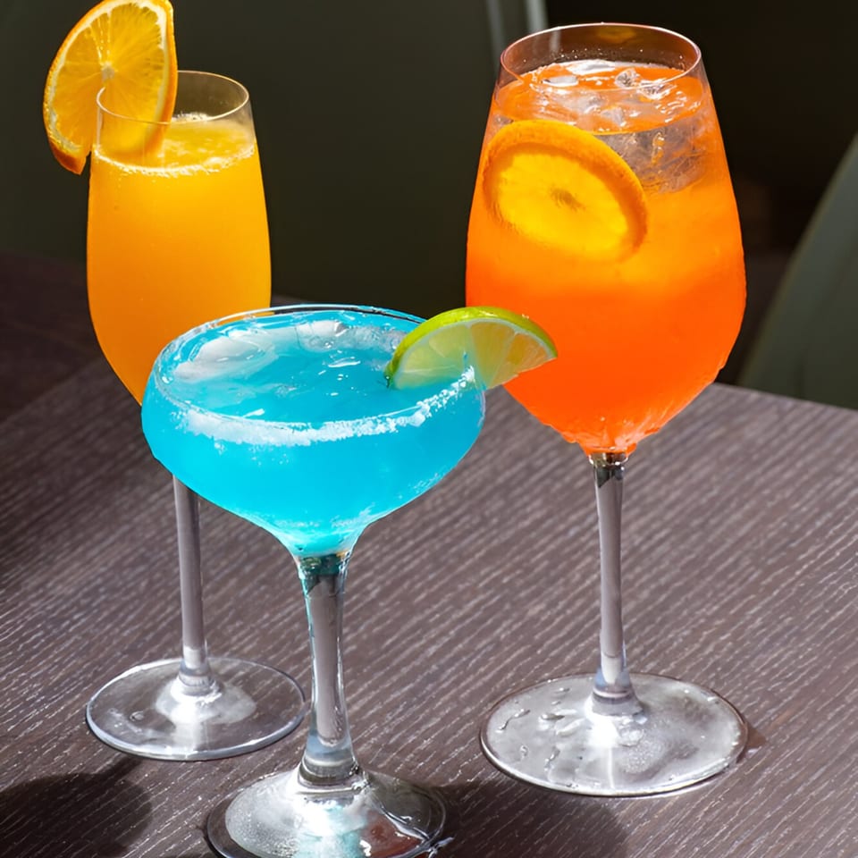 Three vibrant cocktails, two orange and one blue, garnished with citrus slices on a dark table.