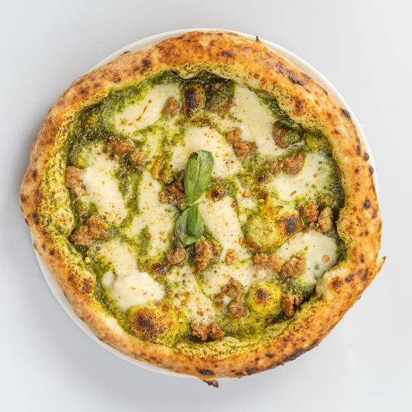 La Fontana's Italian pizza with pesto, mozzarella, sausage, and basil on a white plate.