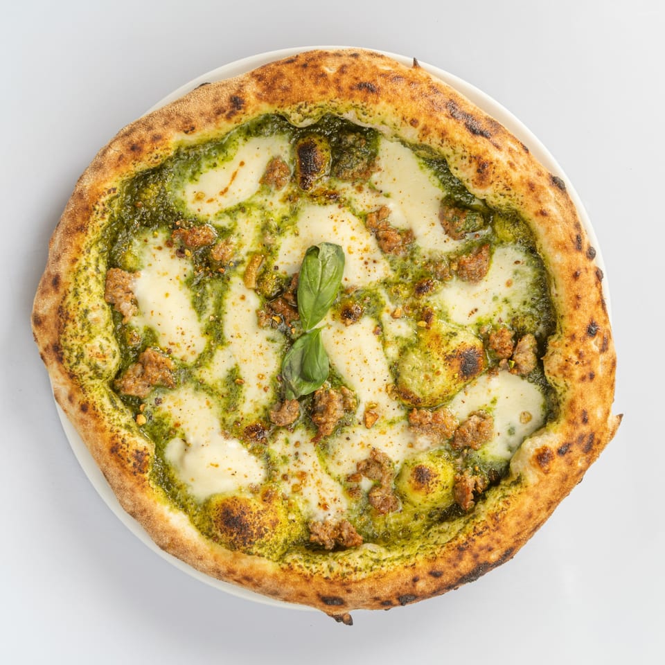 La Fontana's Italian pizza with pesto, mozzarella, sausage, and basil on a white plate.