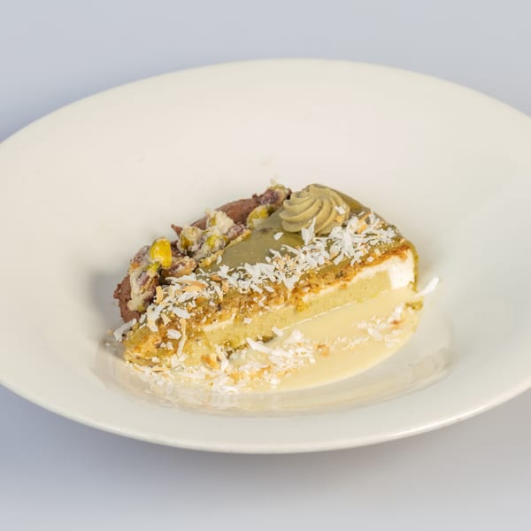 Slice of layered cake with cream, nuts, and shredded coconut on a white plate.